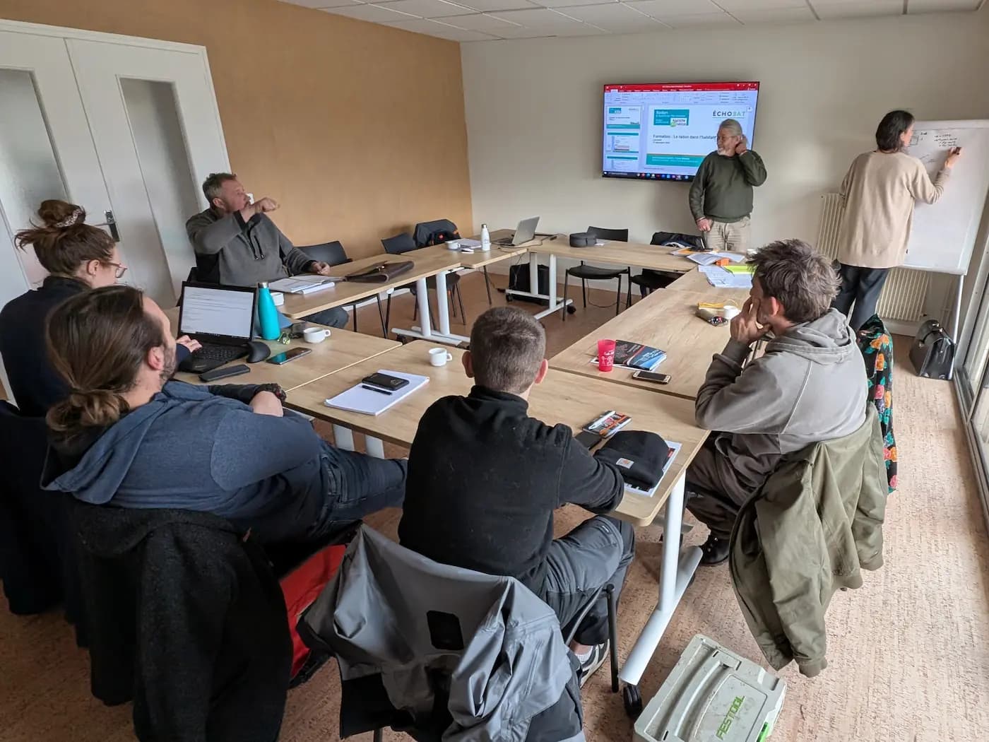 Participants réunis autour de tables pendant qu’une intervenante écrit sur un tableau blanc lors d’une formation sur le radon